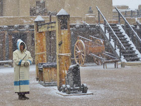 Ranger dressed in period clothing standing inside of Bent's Old Fort Historic Site during a winter snow in La Junta, Colorado.