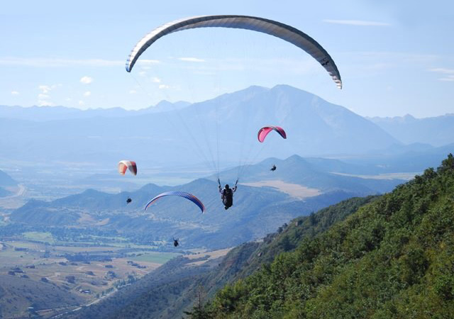 Paragliders with Adventure Paragliding floating of the side of a mountain near Glenwood Springs Colorado. Colorado Paragliding Tandem Flights. In Glenwood Springs, Colorado. Adventure Over the Colorado River Valley.